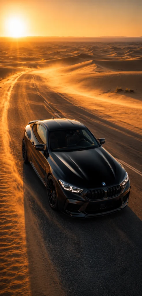 Schwarzer BMW auf einer langen Wüstenstraße während eines goldenen Sonnenuntergangs mit leuchtenden Sanddünen und warmem Abendlicht.