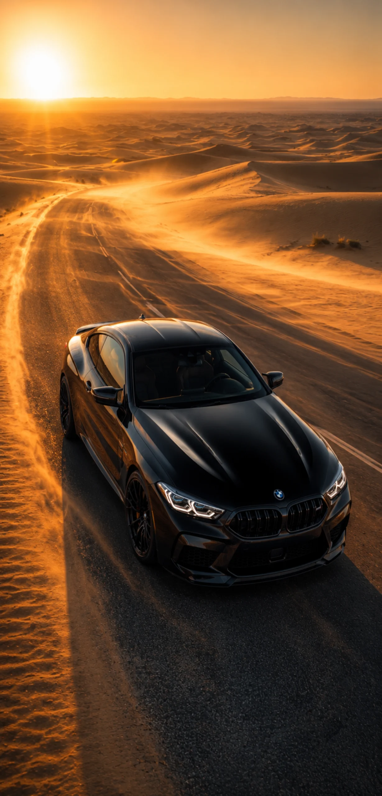 Schwarzer BMW auf einer langen Wüstenstraße während eines goldenen Sonnenuntergangs mit leuchtenden Sanddünen und warmem Abendlicht.
